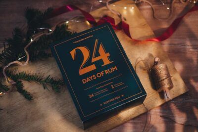 Rumový kalendář 24 Days of Rum - Vánoce a vánoční výzdoba, položený na dřevě s větvičkou
