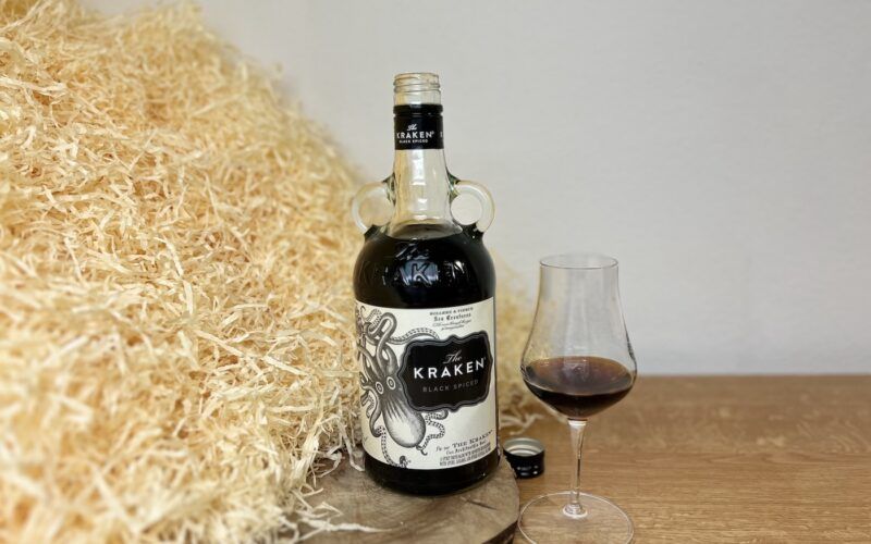 Kraken Black Spiced Rum - láhev, víčko a alkohol ve sklenici na dřevěném podkladu