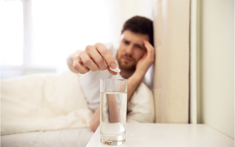Muž s bolestí hlavy si dává lék, sklenici vody na stole