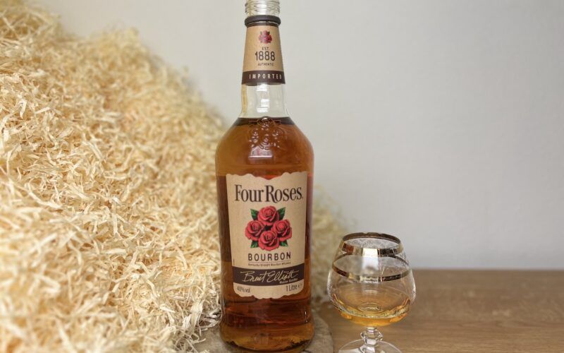 Four Roses Bourbon - degustace, alkohol nalitý ve sklenici a láhev na dřevěném podnosu