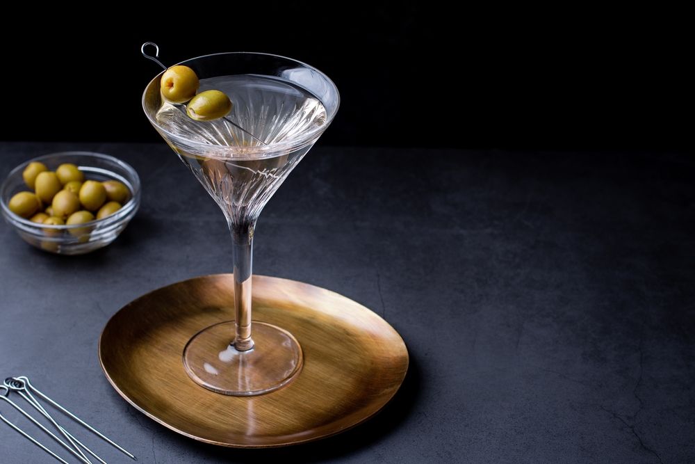 Dirty martini na podtácku s olivami na boku a v drinku na párátku