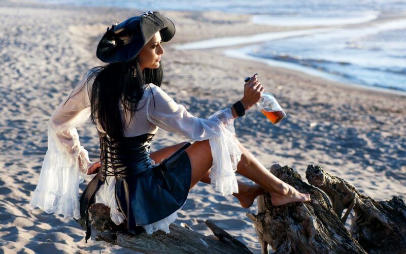 Pirátka s lahví rumu v ruce na písečné karibské pláži